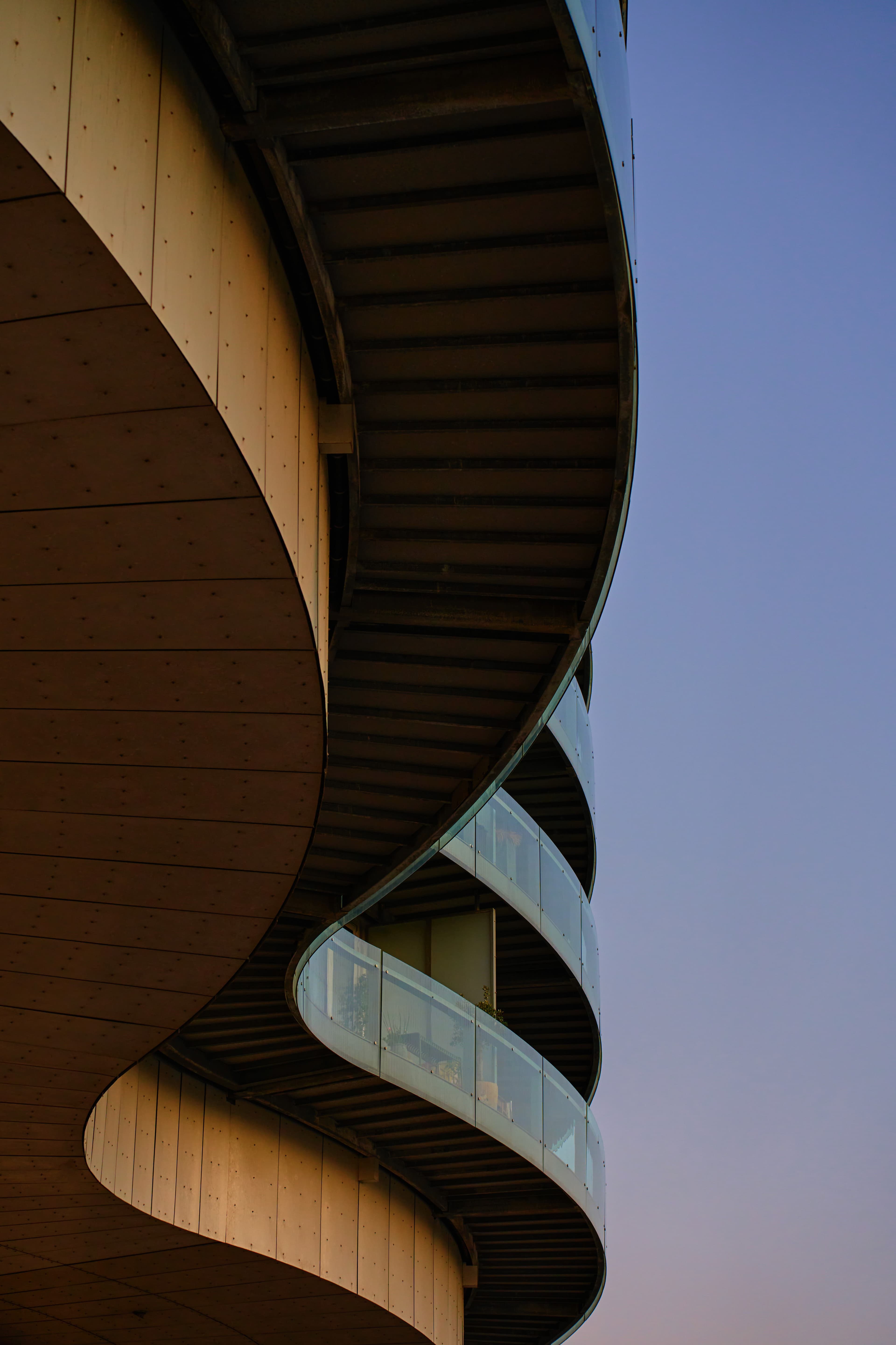 Low-angle view of a modern building with undulating curved balconies and glass railings against a twilight sky.